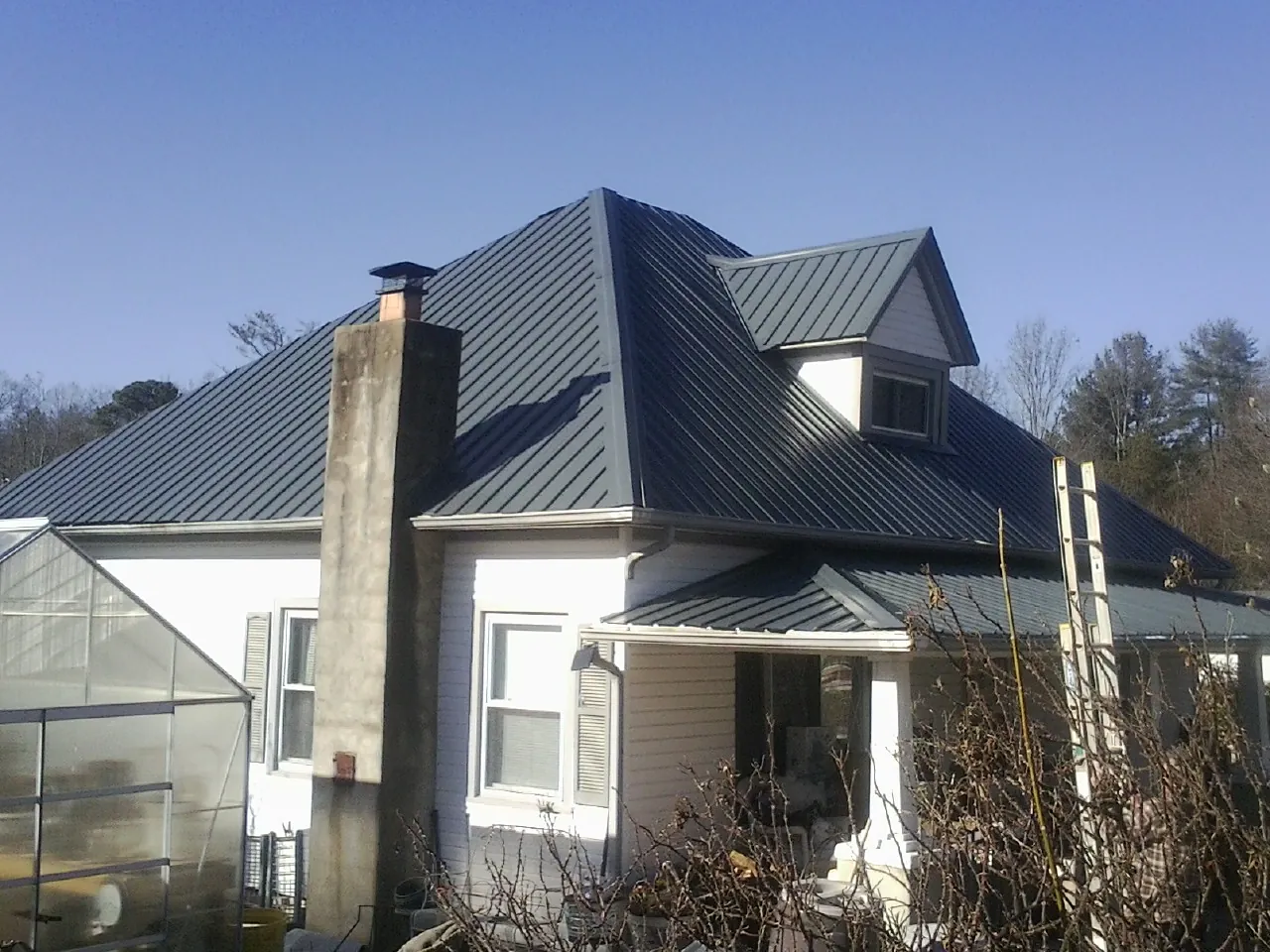 Dark blue standing seam metal roof on a white farmhouse with dormer — Slate & Tile Roof Repair by Roofing Brothers in Mountville