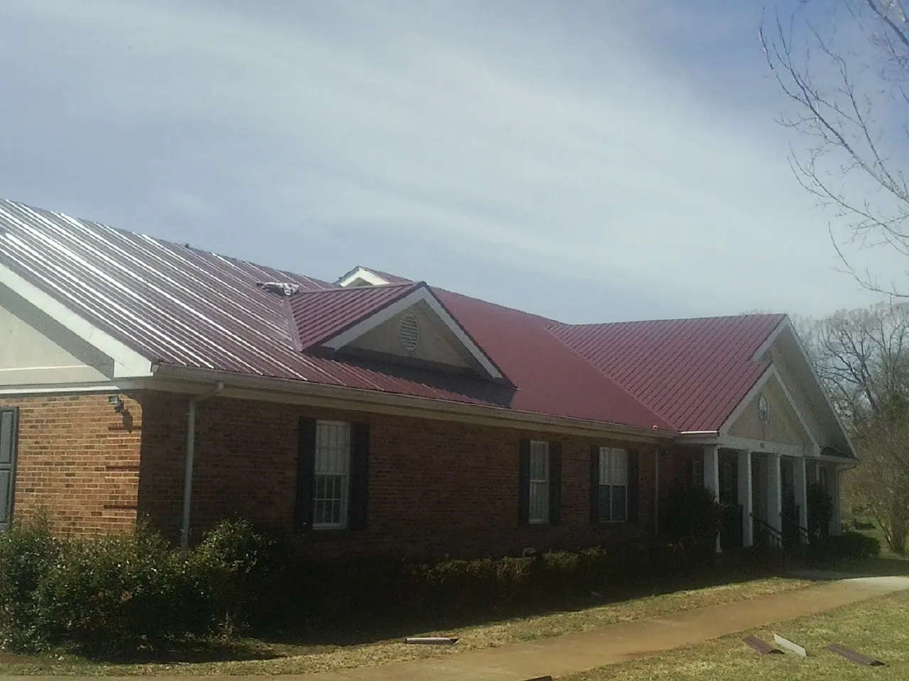 Red metal roof with gabled entries on a long brick building, from a Hail Damage Roof Repair job in Mountville