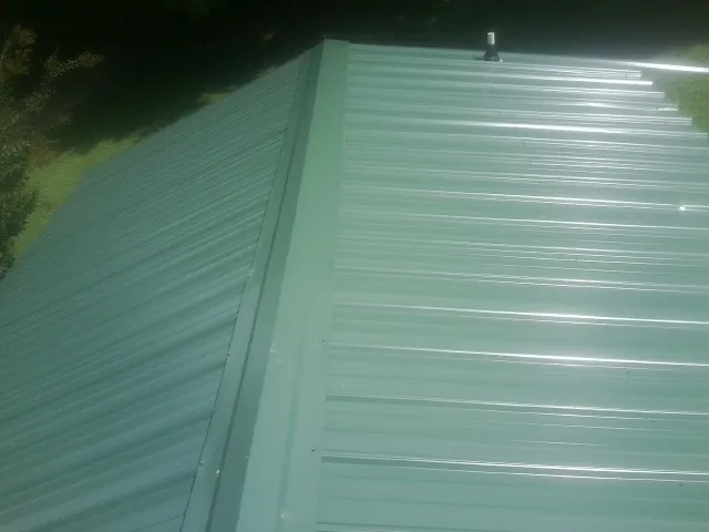New green metal panels meeting at the ridge of a roof — Flat Roof Repair work by our crew in Mountville